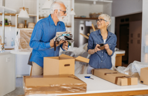 An older couple smiling at each other while they pack moving boxes.