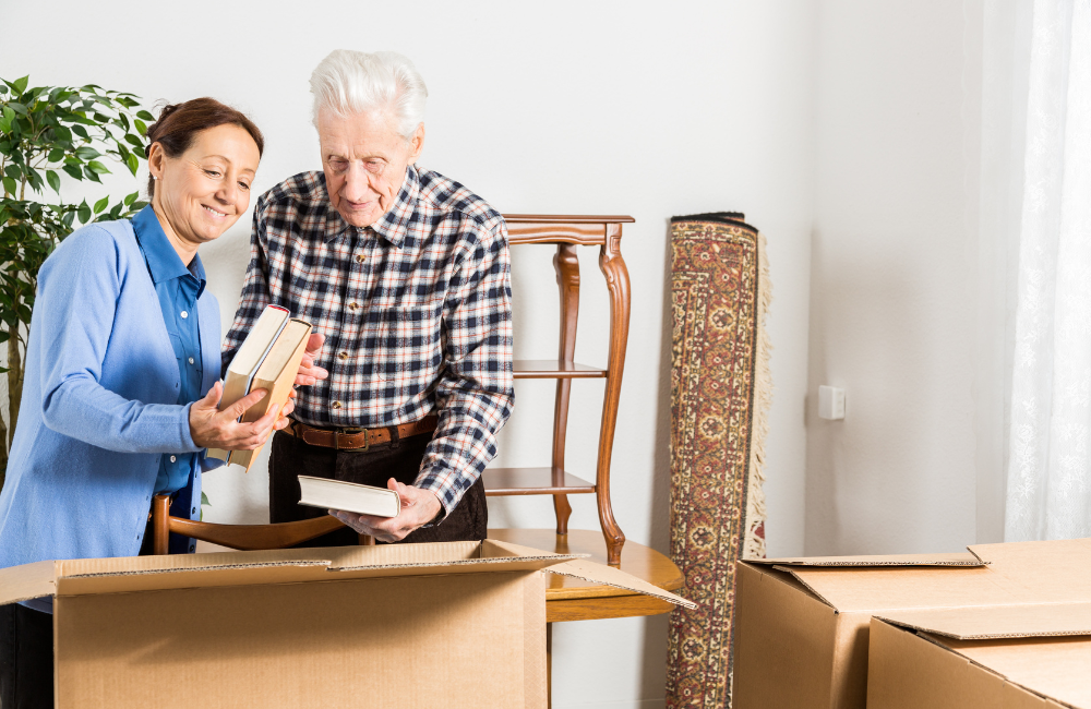 A older man next to a younger woman who is helping to pack books into moving boxes. 