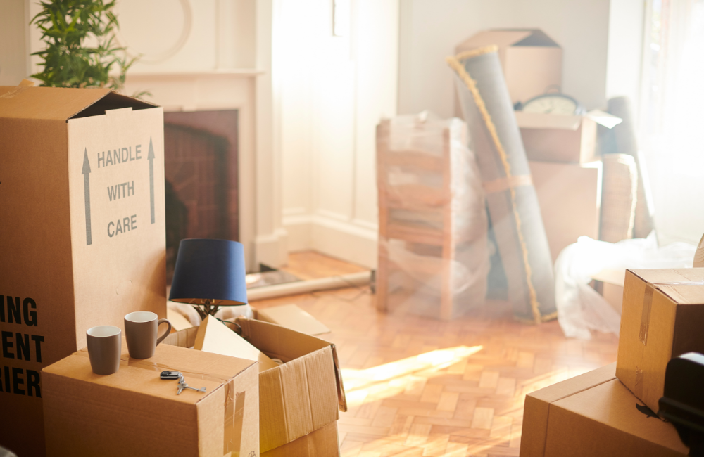 A room with household belonging packed into boxes. There is sunshine streaming in through the window.