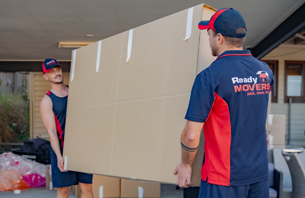 Two Ready Movers removalists carrying a TV box. 