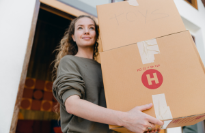 A women carrying a couple of moving boxes out the front door.