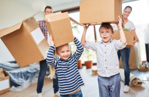 Two children balancing boxes on their head with their father in the background.