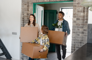 A Mum, Dad and son walking into a new house each carrying a moving box.