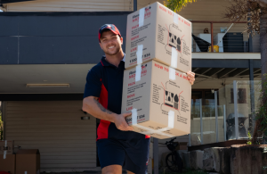 A Ready Movers removalist carrying two boxes out of a house to put onto the truck with a smile on his face.