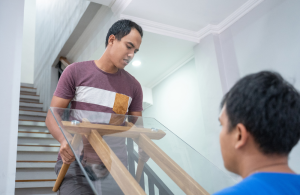 Two men carrying a glass coffee table upstairs.