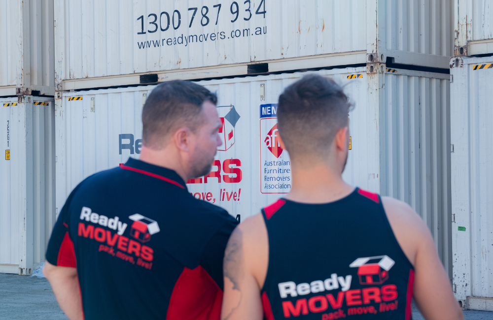 Two Ready Movers removalists standing in front of shipping containers with 'Ready Movers' written across the front. 